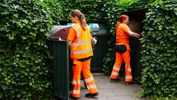Zwei Kolleginnen in Orange stellen die geleerten Mülltonnen zurück