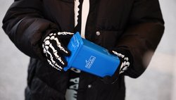 Verkleidets Skelett mit einer Mini-Papiertonne in der Hand