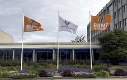 Bild von drei gehissten Fahnen vor der Hauptgebäude der Stadtreinigung Hamburg: In der Mitte ist die Flagge der Stadtreinigung gehisst, links und rechts neben je eine orangefarbene Flagge mit einem Herzen in Regenbogenfarben, darunter der Schriftzug: Bunt wie Hamburg