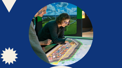 Menschen besuchen eine Ausstellung mit Infotafeln, einem großen Ausstellungstisch und einer Landschaftsprojektion an der Wand.